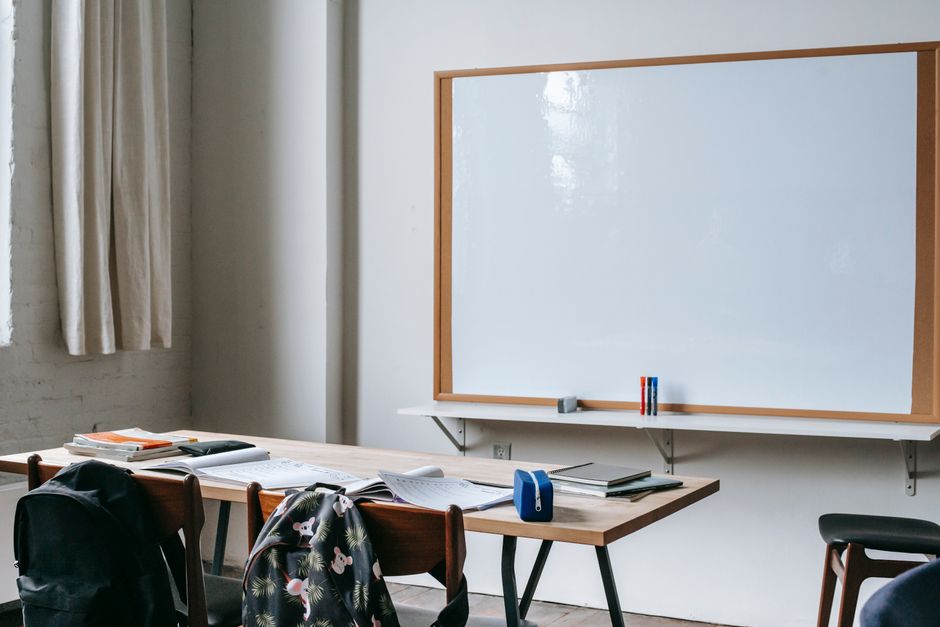 Classroom interior with whiteboard against student desk with notebooks and stationery in modern school
